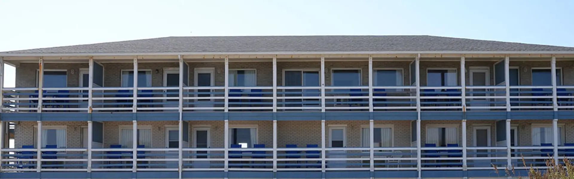 The Blue Heron Motel seen from the beach — three storeys of guest rooms, each with a balcony of blue panels and blue chairs behind white railings