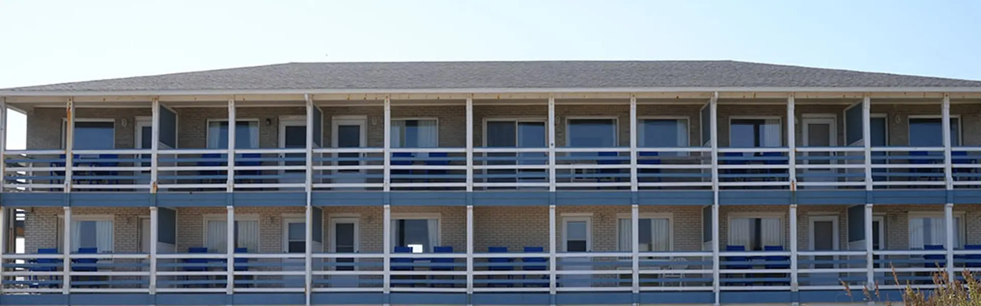 The Blue Heron Motel seen from the beach — three storeys of guest rooms, each with a balcony of blue panels and blue chairs behind white railings