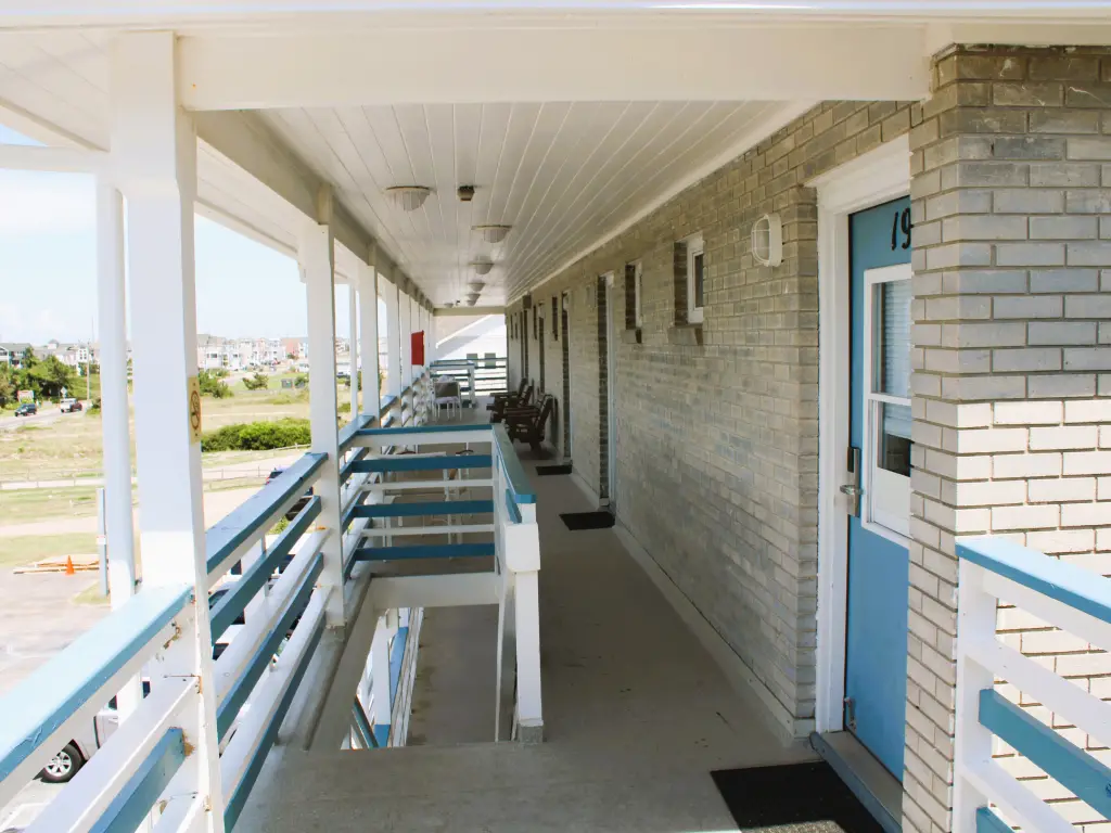 An upper-floor walkway at the Blue Heron Motel, with blue room doors, white and blue railings and chairs set outside each room