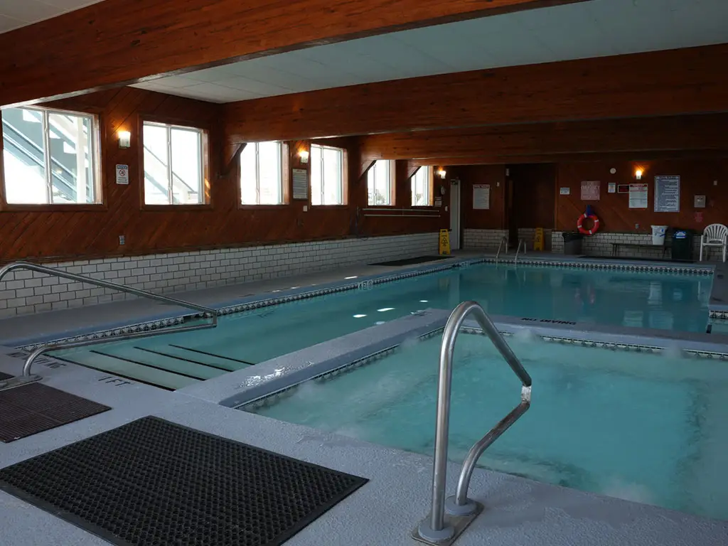 An indoor swimming pool with a hot tub, surrounded by wood-panelled walls with windows and white tiled wainscoting