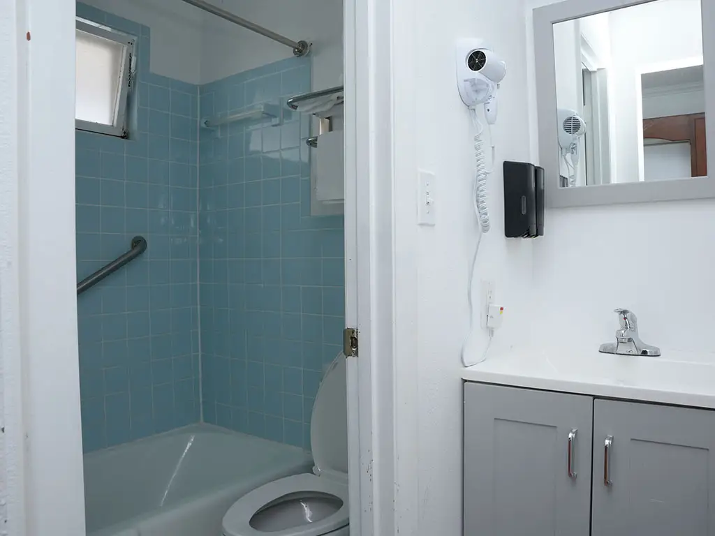 A bathroom with a toilet, a bathtub with blue tiled walls, and a vanity with a sink and grey cabinets