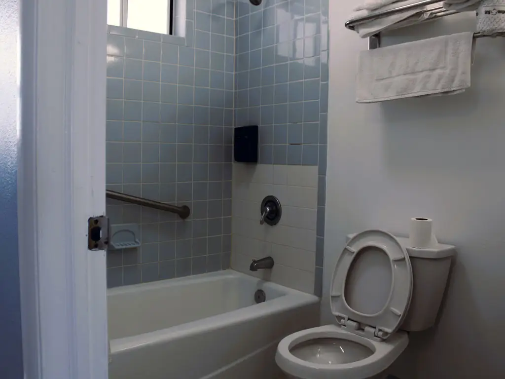 A bathroom with light blue tiled walls, a white bathtub, and a toilet with the lid up
