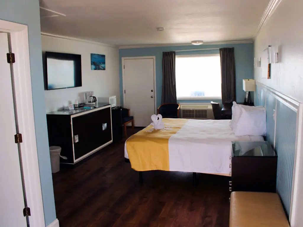 A guest room with a bed, a desk, a television, a microwave, a coffee maker and a small refrigerator