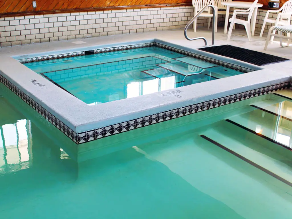 An indoor swimming pool with a smaller square hot tub, surrounded by white brick walls and wood panelling