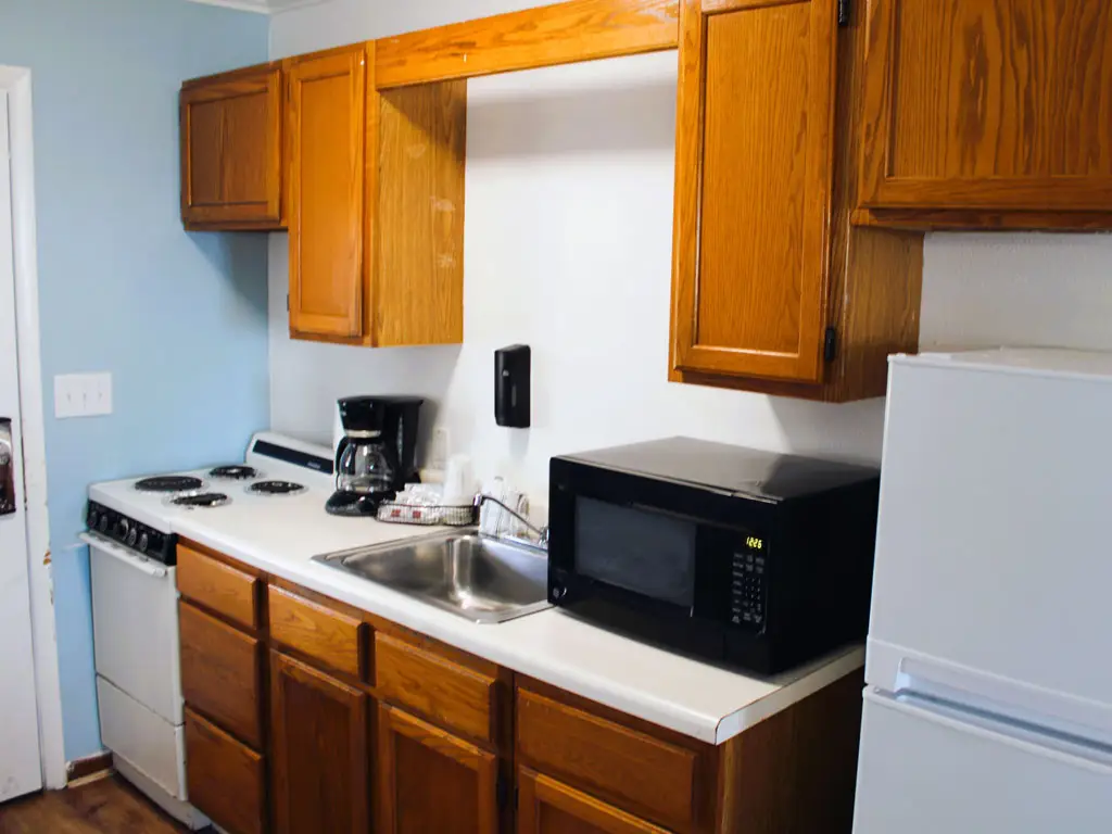 A kitchenette with wooden cabinets, a white stove, a microwave, a coffee maker and a refrigerator
