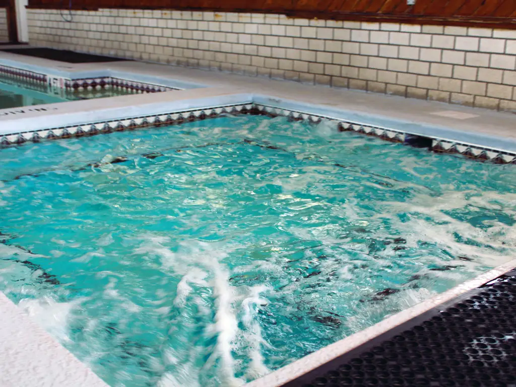 Two rectangular indoor pools with light blue water, one in the foreground and one further back, are surrounded by a tiled wall