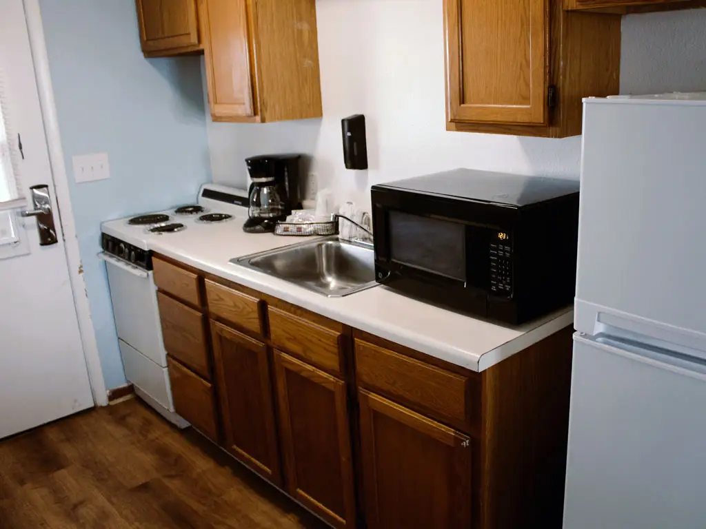 A kitchenette with a white stove, a coffee maker, a microwave, a sink, and a white refrigerator