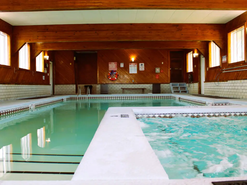 An indoor swimming pool with a separate hot tub, surrounded by wood-panelled walls and white brickwork