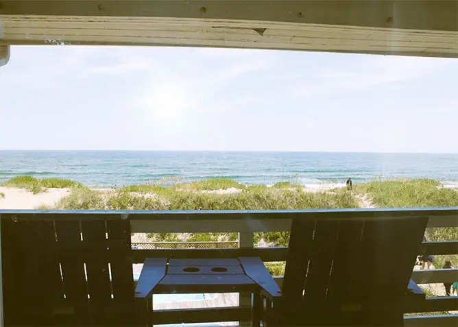 The view from a guest balcony — two blue chairs and a small table, looking past the dunes to the Atlantic